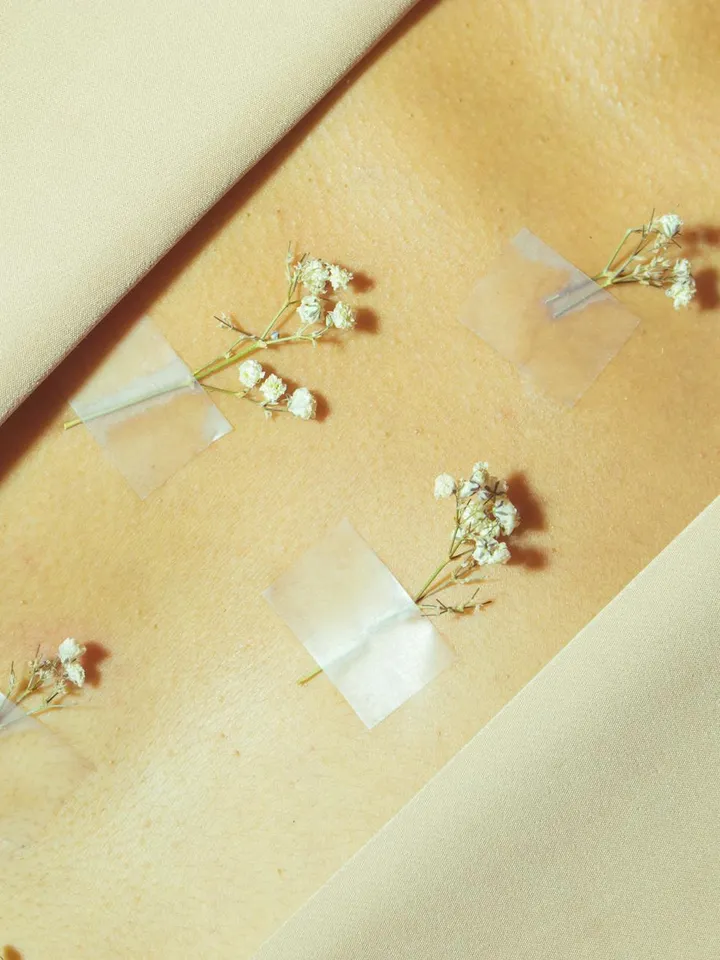 Minimalist photo of tiny white baby's breath flowers taped onto a warm beige background, evoking a clean, ingredient-focused aesthetic.