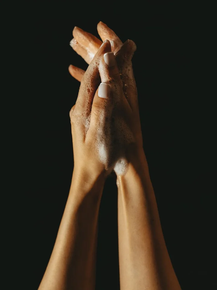 Two hands covered in white soap lather against a dark background, illustrating hygiene and caution before using chemical skincare agents.