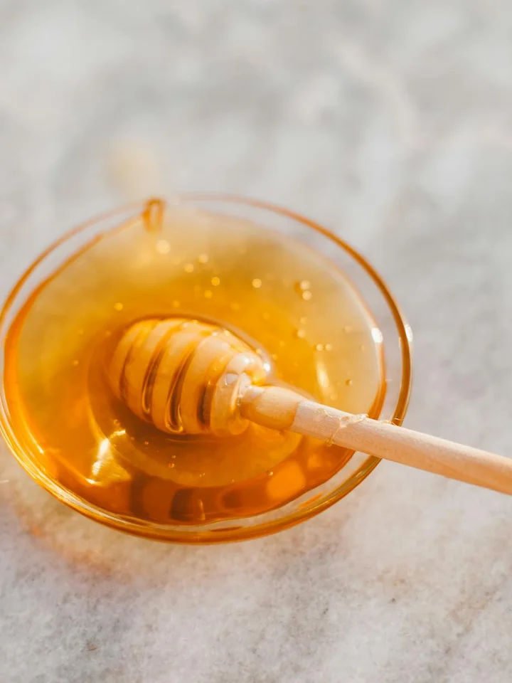 Golden honey in a glass bowl with a wooden honey dipper