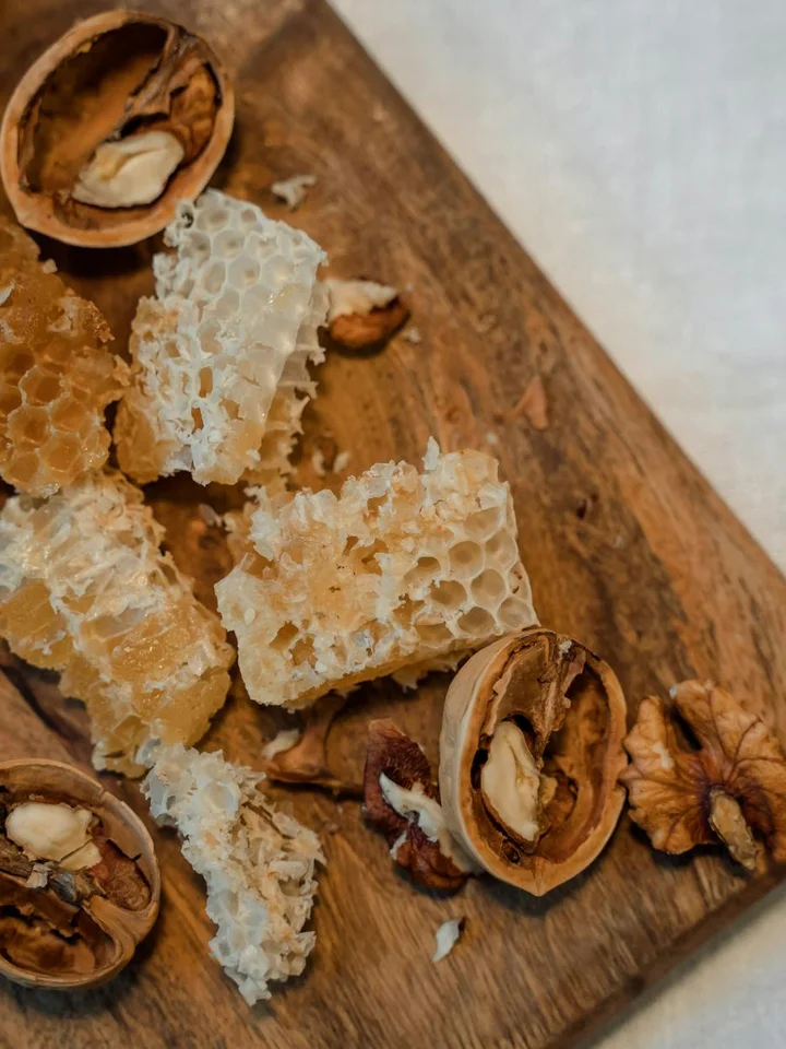 Close-up of honeycomb pieces on a wooden surface with cracked walnut shells