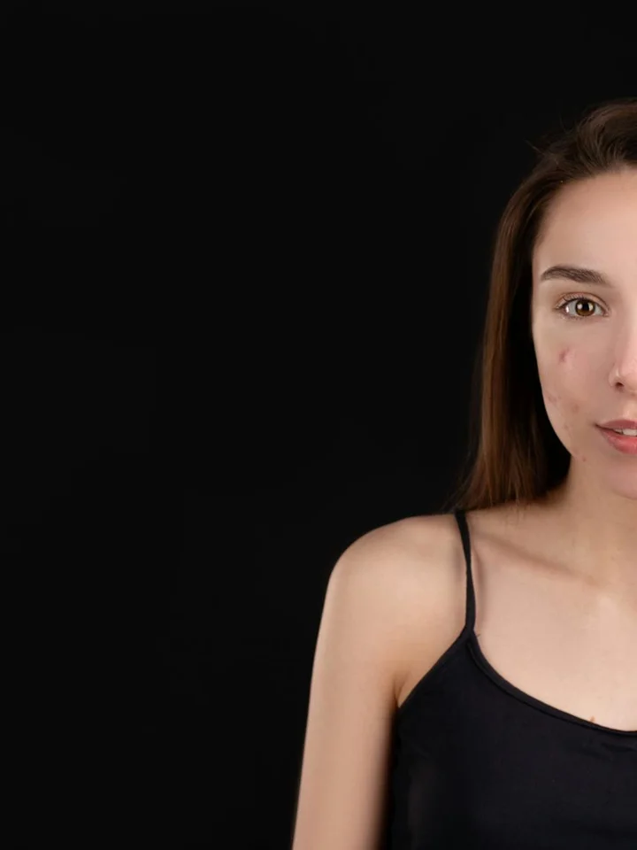 Portrait of a young woman with fair skin wearing a black sleeveless top against a dark background