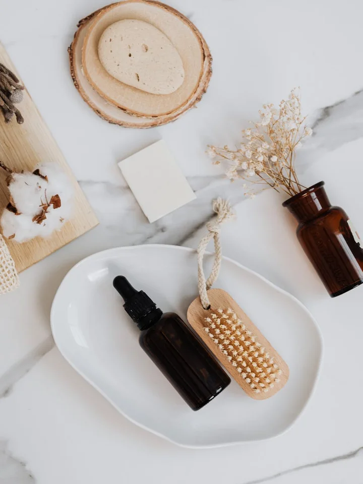 Skincare flat lay on a marble surface, showing a brown glass dropper bottle, a wooden tag, and dried botanicals.