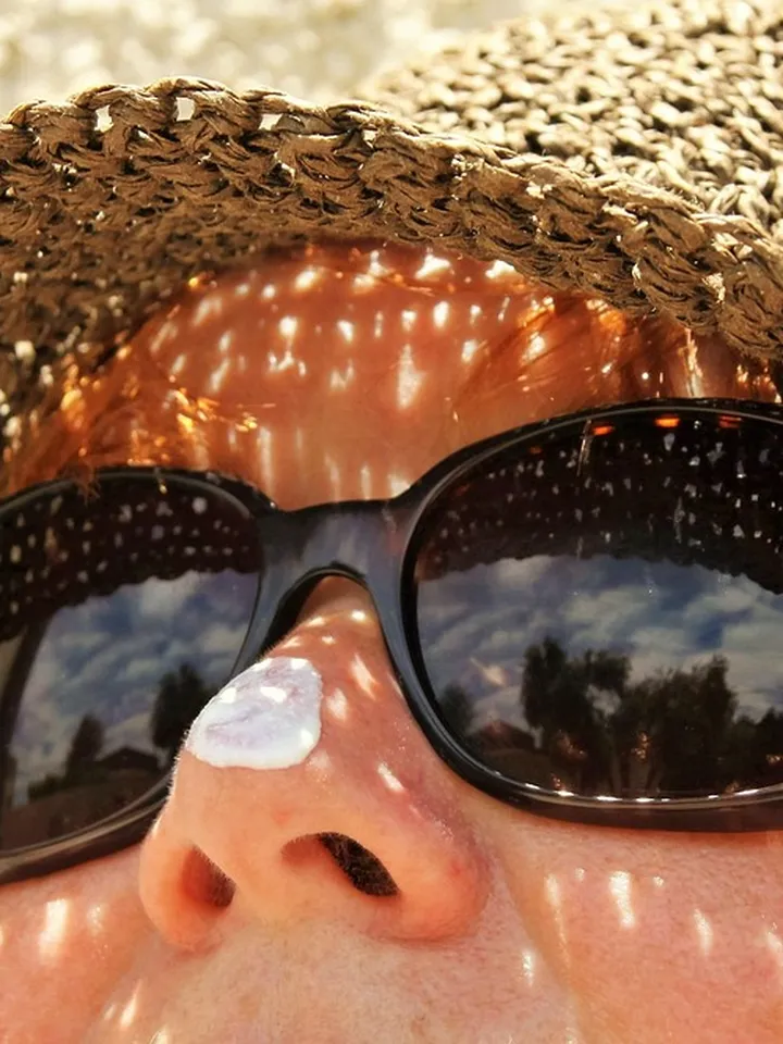 Close-up of a person wearing a straw hat and dark sunglasses with dappled sunlight on their face.