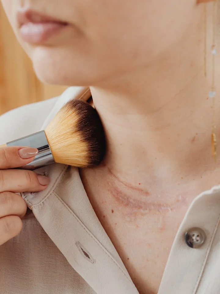 Close-up of a person applying concealer with a brush near the neck and jawline, highlighting skin texture and patch-testing area