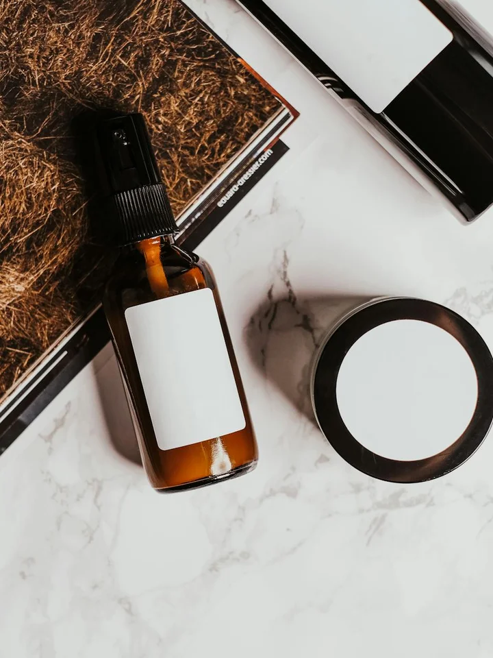 Brown glass dropper bottle and a round cosmetic jar placed on a marble surface, with other skincare items in the background.