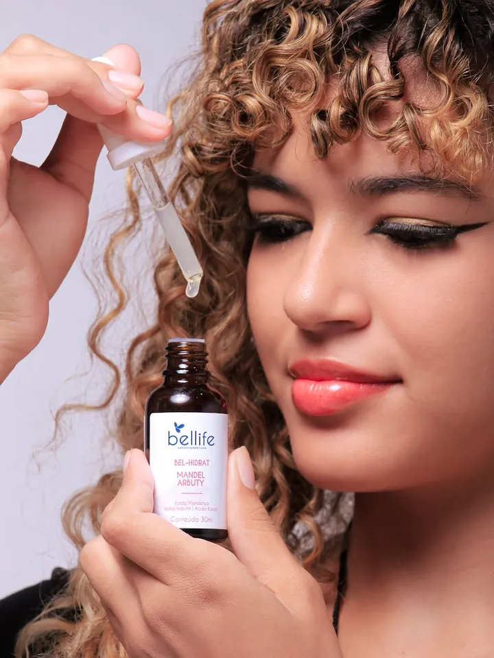 Close-up of a person using a dropper to apply serum from a brown glass bottle.