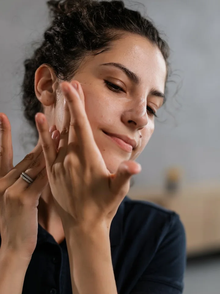 Close-up of a person applying skincare serum to their face with a gentle expression, highlighting mindful, ethical formulation.