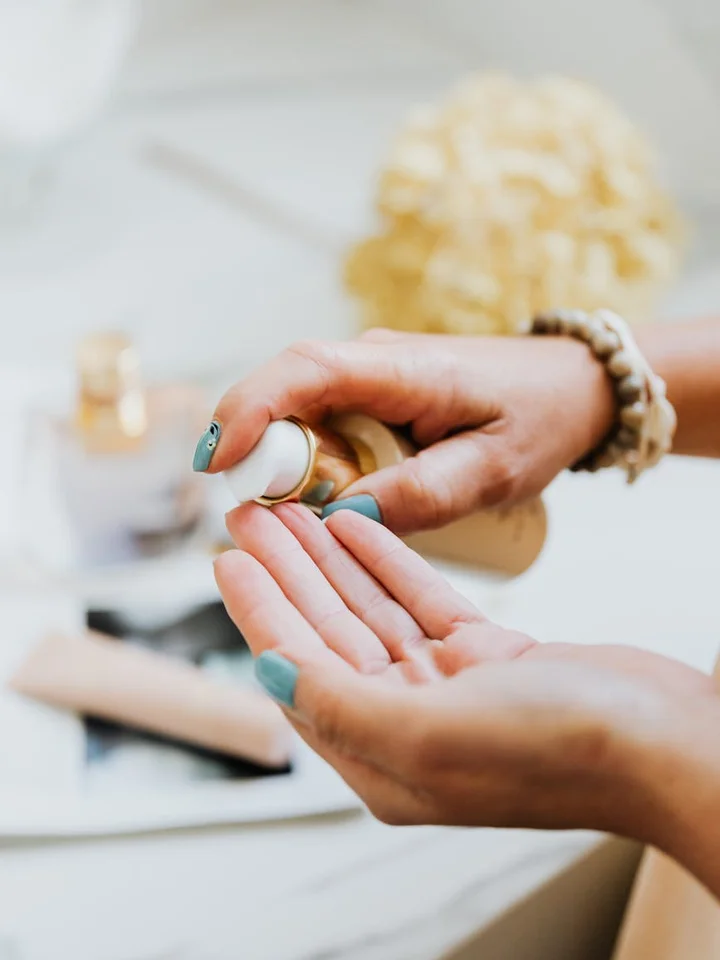 Close-up of hands dispensing a skincare product onto the palm, with blurred bottles in the background.