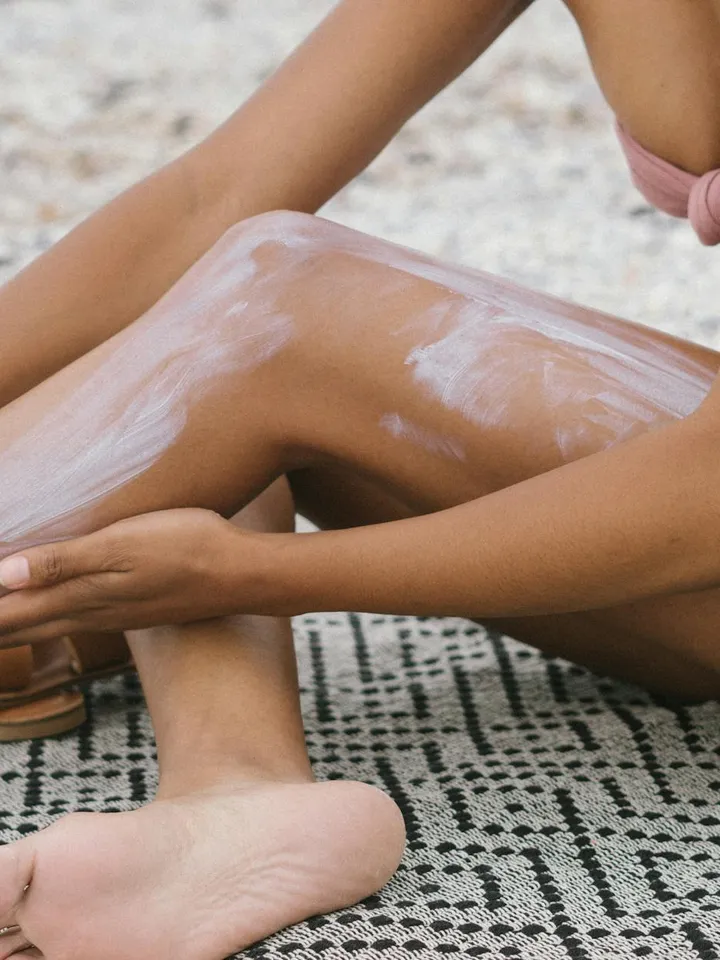 Person applying a white cream onto their leg while seated outdoors