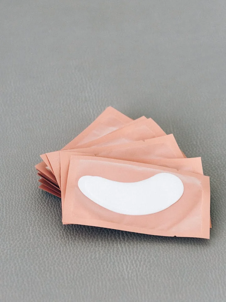 Several pink sachets with white curved patches resembling lip masks arranged on a gray surface.