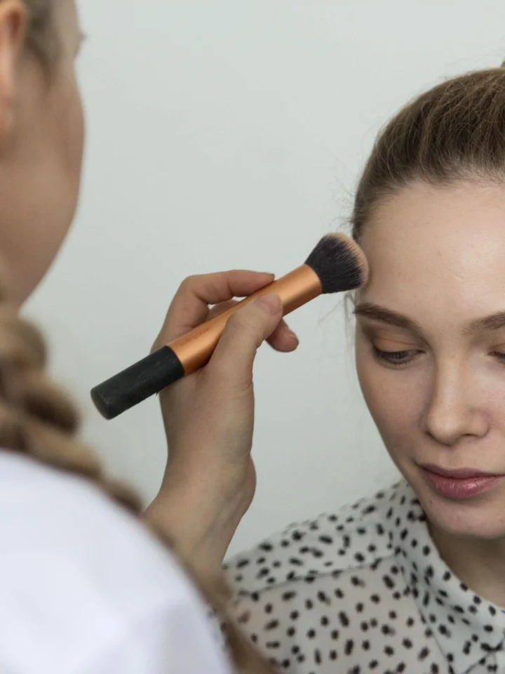 Close-up of a makeup artist applying makeup with a brush to a model's face
