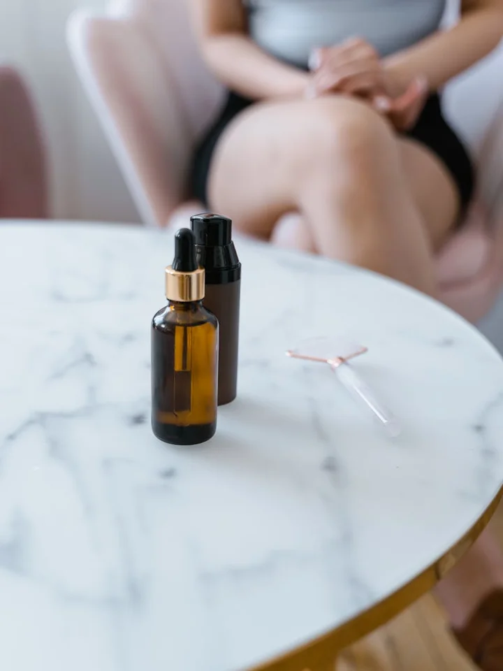 Two amber dropper bottles on a marble table with a blurred person in the background, representing skincare product selection.