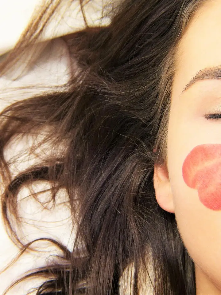 Close-up of a woman's face with long dark hair, showing a red circular patch on her cheek