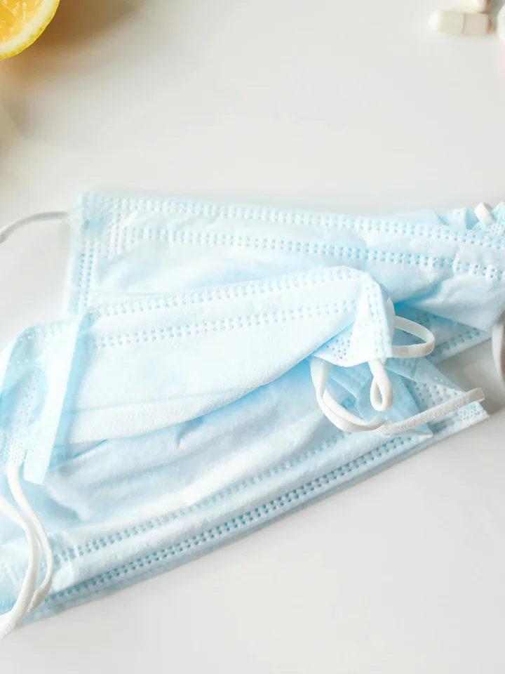 Blue disposable face masks on a white surface with a lemon slice partially visible in the top-left corner.