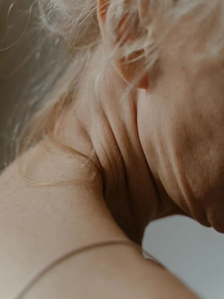 Close-up of aging neck skin with visible wrinkles and fine texture; hair strands are faintly visible in the background.