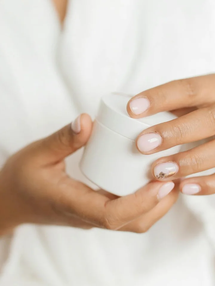 Close-up of hands holding a small white skincare jar against a light background
