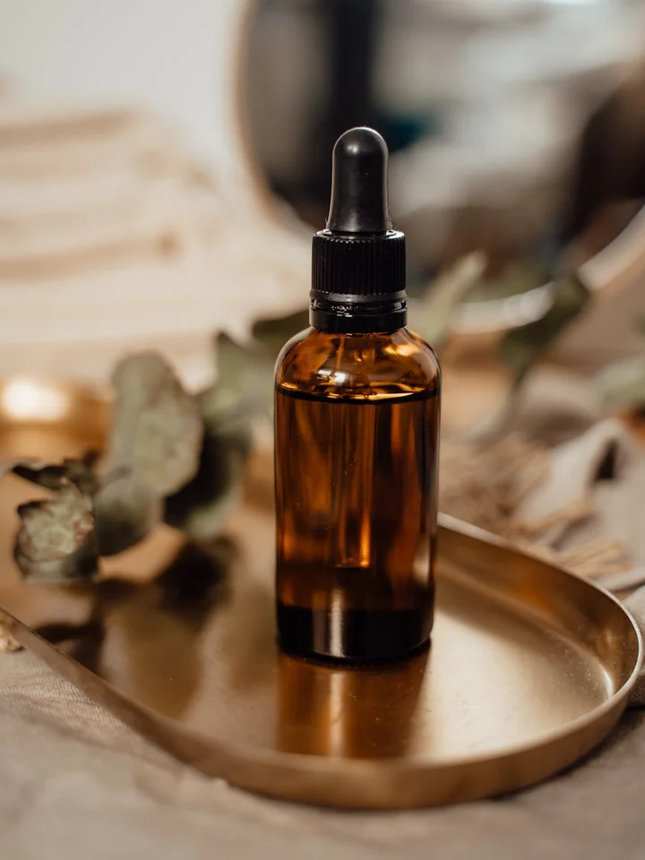 Close-up of an amber glass dropper bottle on a brass plate with a soft-focus background, suggesting a skincare routine.
