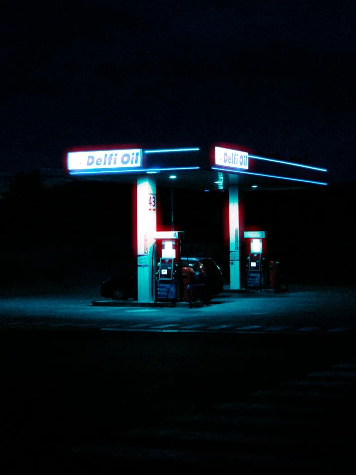 Nighttime gas station with blue neon lighting and fuel pumps.