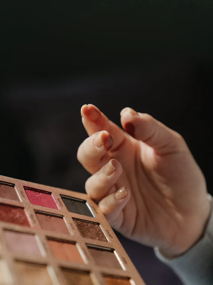 Close-up of a hand hovering over a warm-toned NYX eyeshadow palette with multiple shades.