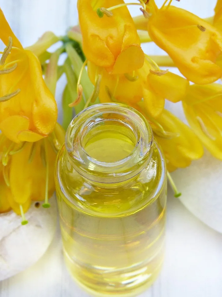 Close-up of a glass bottle filled with yellow oil, with bright yellow flowers in the background.