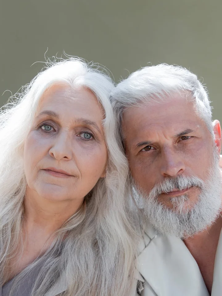 Close-up of an older couple with gray hair looking at the camera with neutral expressions.