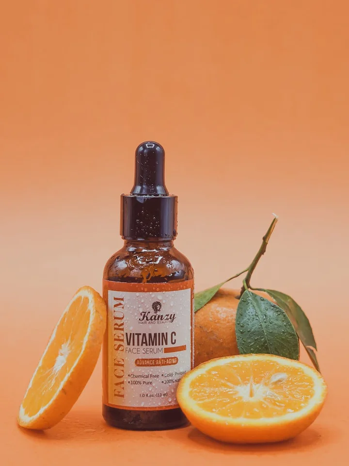 Dropper bottle of Vitamin C serum next to halved oranges on an orange background