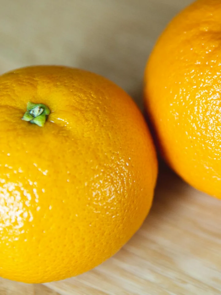 Two bright oranges on a light wooden surface