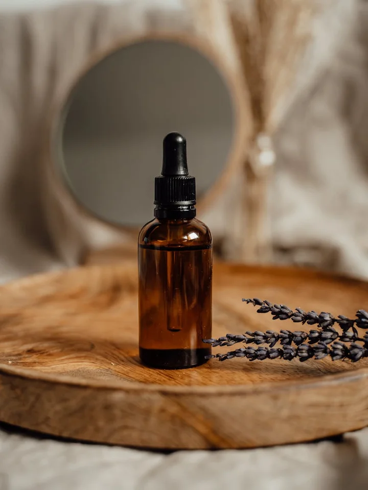 Brown dropper bottle on a wooden tray with a sprig of lavender; blurred background