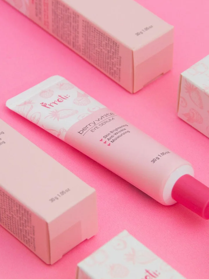 Close-up of pastel pink cosmetic tubes and boxes arranged on a pink background.