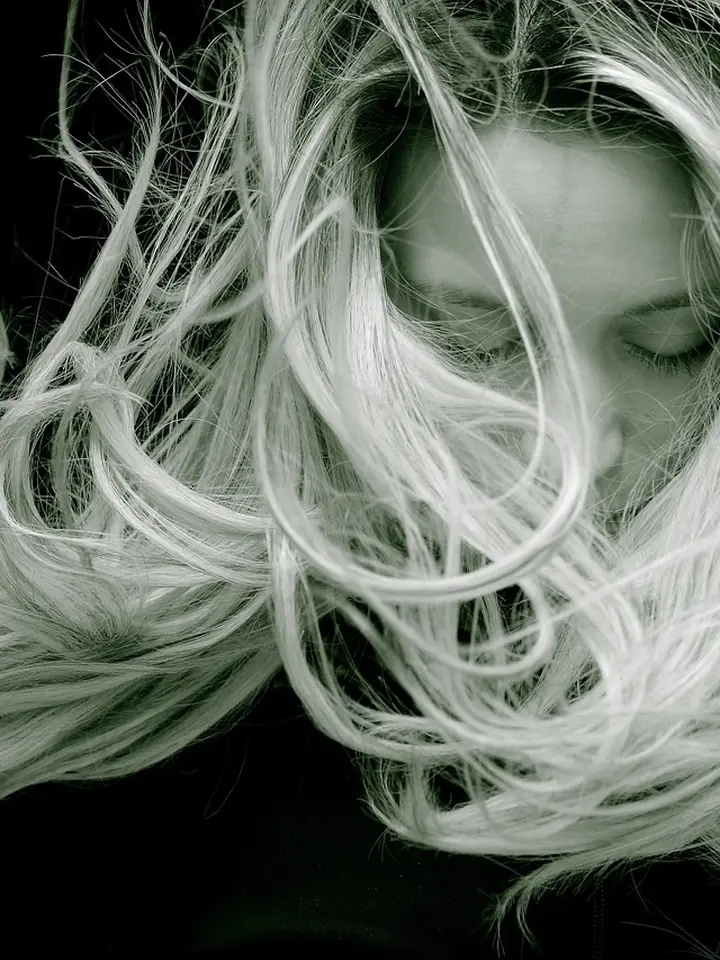 Close-up portrait of a person with long hair flowing across the face, obscuring facial features.