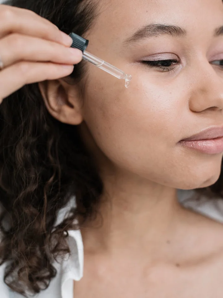 Close-up of a woman applying serum with a dropper to her cheek, illustrating the strengthening phase after microneedling.