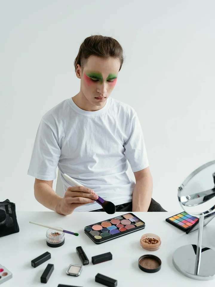 Person applying makeup with a brush, surrounded by colorful makeup palettes and powders on a white table