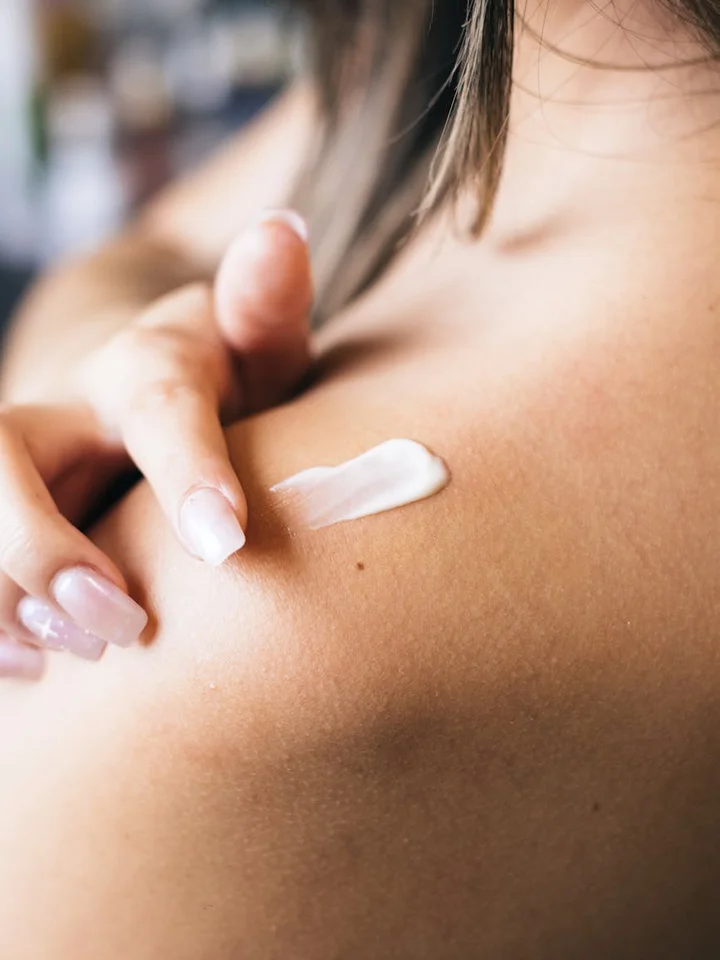Close-up of a hand applying white cream to a woman's shoulder
