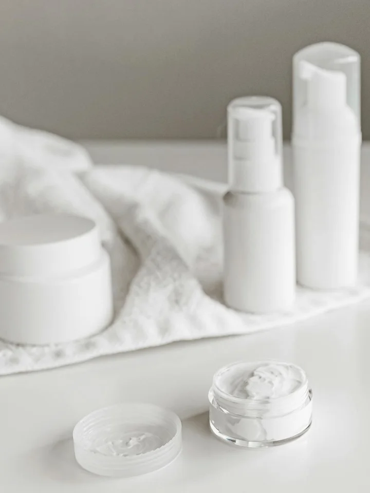 Close-up of white skincare bottles and a small open jar on a clean white surface, representing skincare products involved in purging discussions.