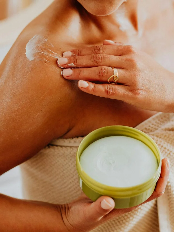 A person applying cream from a green-lidded jar to their shoulder.