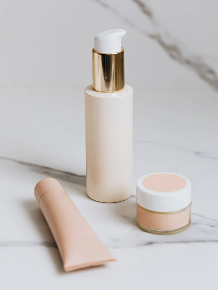 Skincare products including a pump bottle, a small jar, and a tube on a marble surface, representing retinoid formulations.