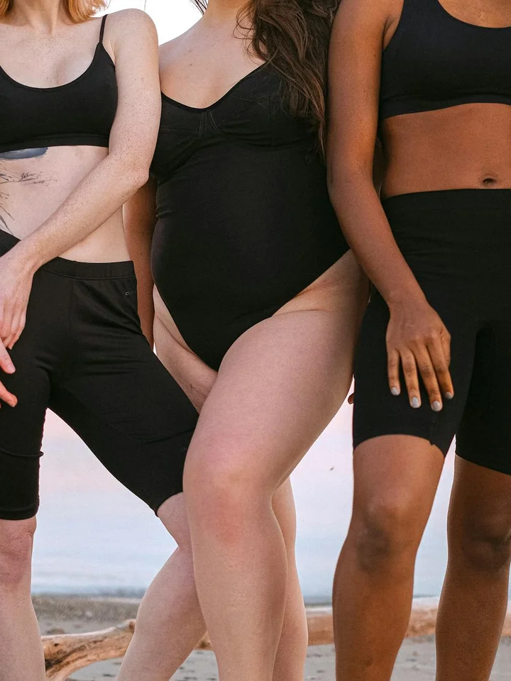Three people wearing black athletic outfits standing on a beach.