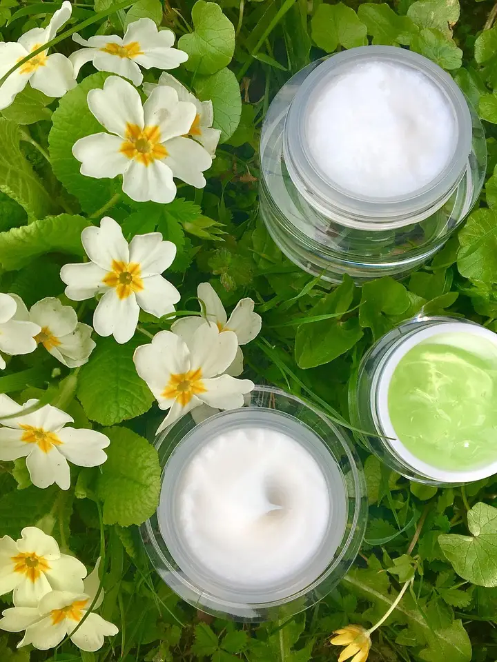 Jars of cream on green leaves and white flowers, illustrating skincare layering and retinol compatibility.
