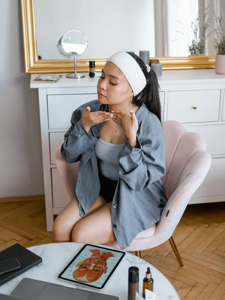 A woman with a white headband applying skincare at a vanity, contemplating safety warnings before using Rhode skincare products.