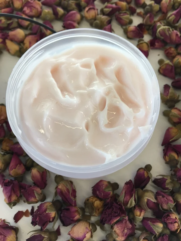 A small jar of pale pink cream surrounded by dried rose petals.