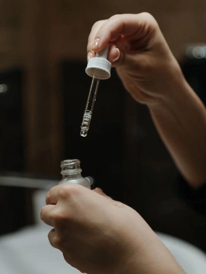 Close-up of a hand using a dropper to dispense serum into a bottle, illustrating careful skincare application.