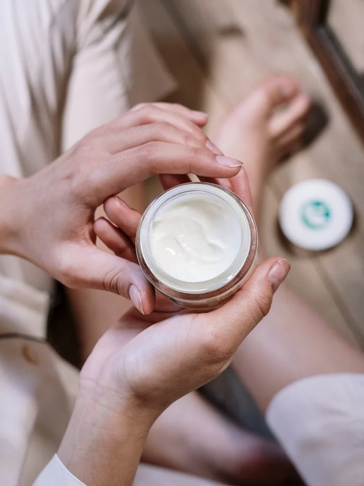 Close-up of hands holding an open jar of white cream, ready to apply skincare.