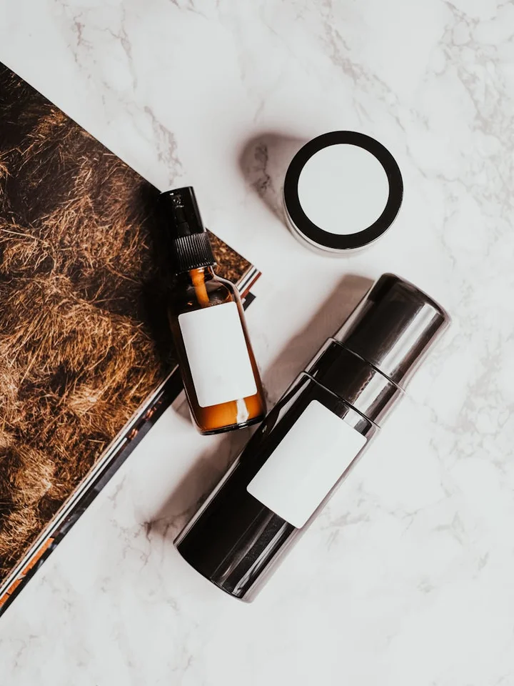 A small skincare setup featuring a dropper bottle, a pump bottle, and an open round container placed on a marble surface, representing products to be used for combining niacinamide and tretinoin.