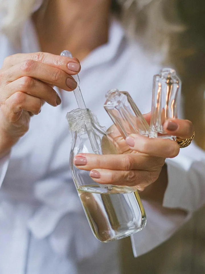 Close-up of hands holding clear glass dropper bottles with liquid, used for skincare serums.