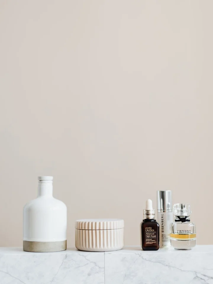 Minimalist skincare setup with a white bottle, ribbed jar, and small brown and clear dropper bottles on a marble surface