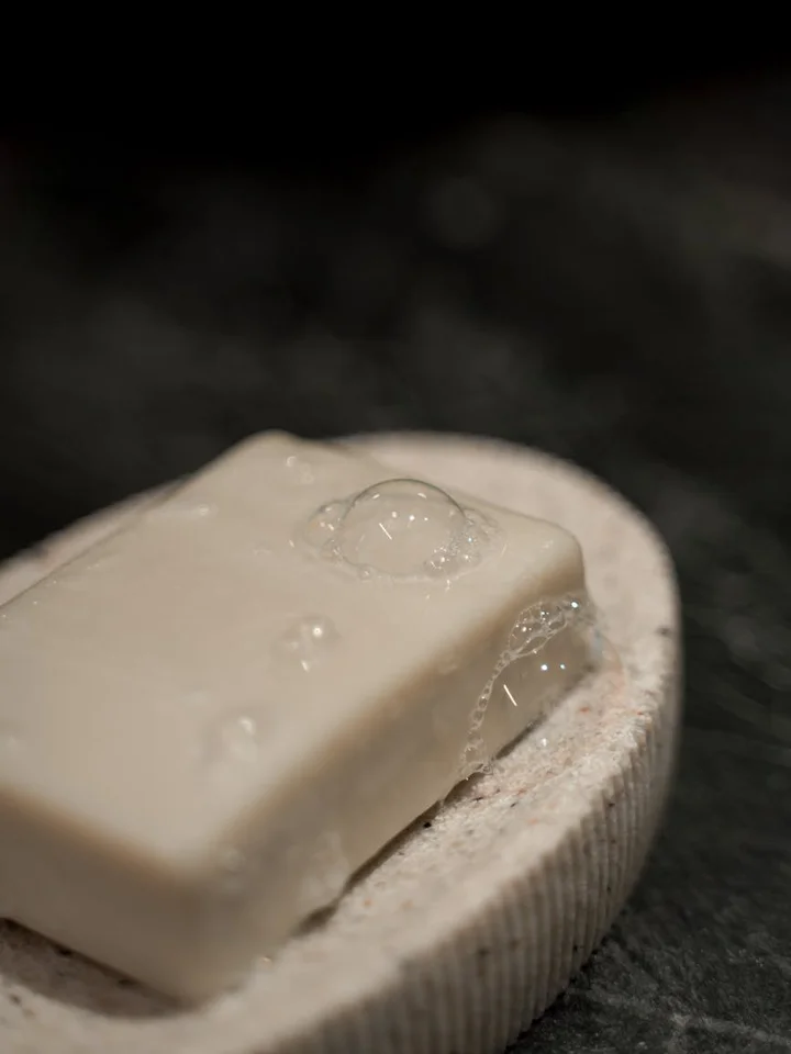 Close-up of a pale bar of soap resting on a textured circular dish.