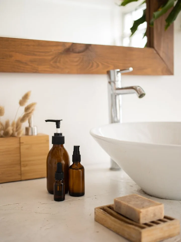 Minimalist bathroom sink area with brown glass bottles and a bar of soap on a wooden tray beside a white sink.