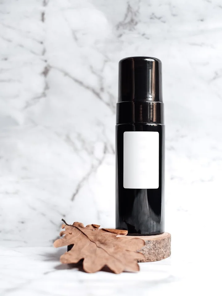 Black pump bottle on white marble surface with a dried brown leaf, suggesting skincare layering.