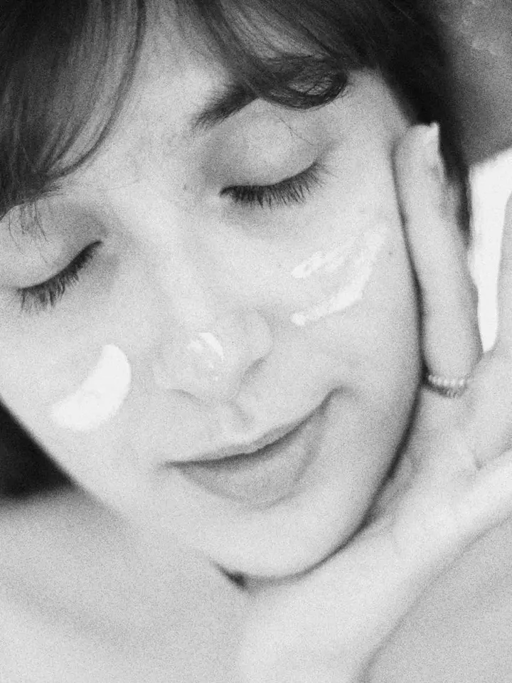 Close-up of a person with a dollop of skincare cream on the cheeks, preparing to apply product