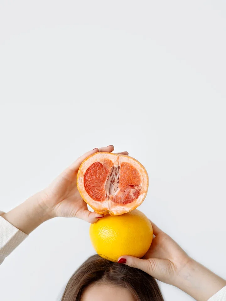 Two hands hold a halved grapefruit atop a whole lemon against a clean white background.